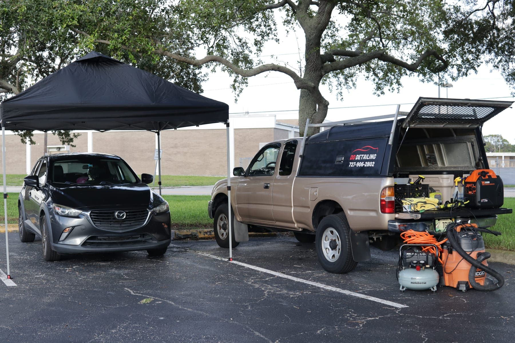 DD Detailing on-site setup: a black tent over a car beside the DD Detailing truck, with the generator, vacuum and compressor